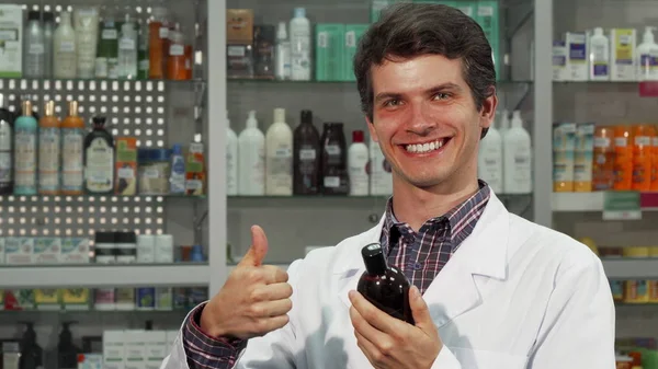 Farmacêutico alegre mostrando polegares para cima enquanto trabalhava na farmácia — Fotografia de Stock