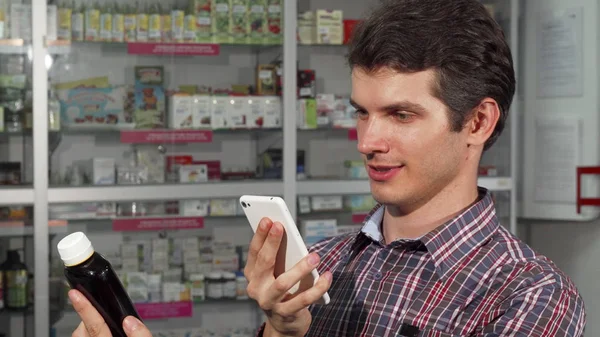 Mladý muž pomocí chytrého telefonu při nákupu v lékárně — Stock fotografie