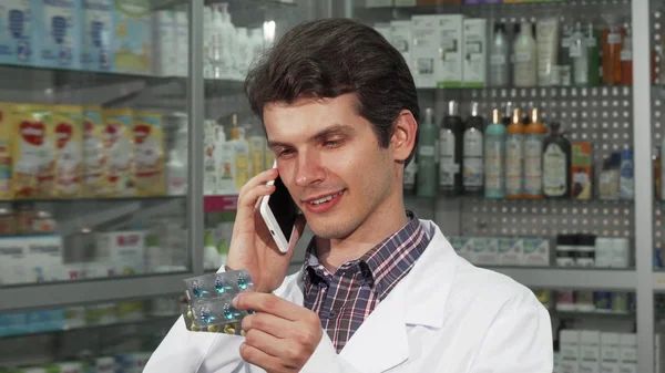 Clínico hablando por teléfono, sosteniendo dos ampollas de pastillas — Foto de Stock
