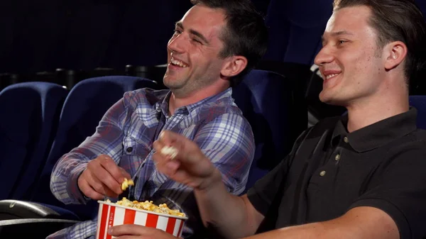 Male friends eating popcorn and laughing while watching comedies at the cinema — Stock Photo, Image