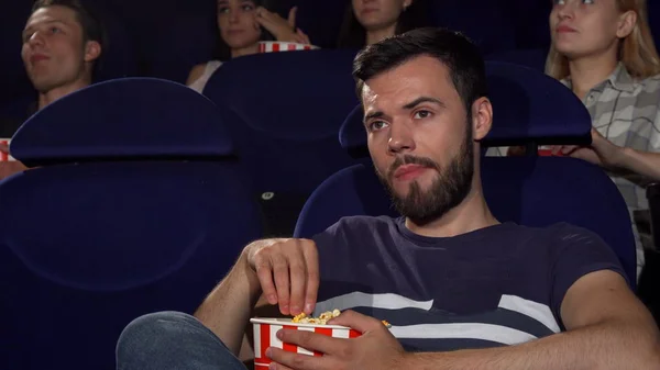 Jovem atraente comendo pipocas durante filme chato no cinema — Fotografia de Stock
