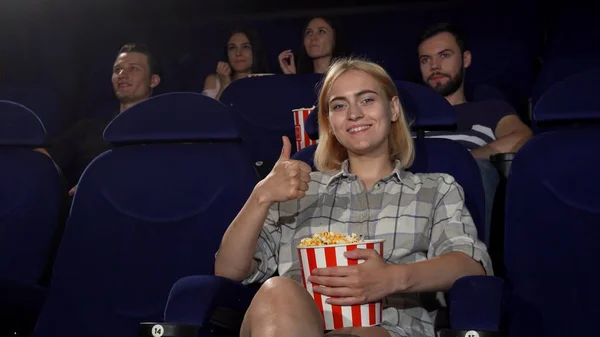 Junge attraktive Frau lächelt und zeigt Daumen hoch im Kino — Stockfoto