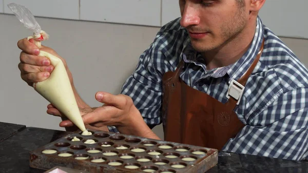 Jovem confeiteiro masculino adicionando enchimento de baunilha em moldes de chocolate — Fotografia de Stock