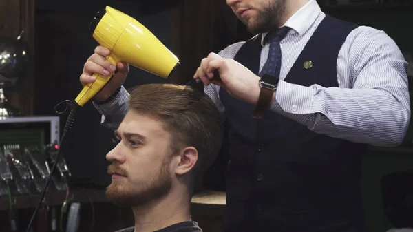 Jovem bonitão recebendo seu cabelo seco por um barbeiro — Fotografia de Stock