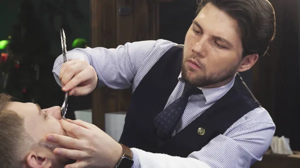 Профессиональный парикмахер бреет своего клиента бритвой — стоковое фото