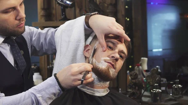 Красивому молодому человеку сбривают бороду в парикмахерской — стоковое фото