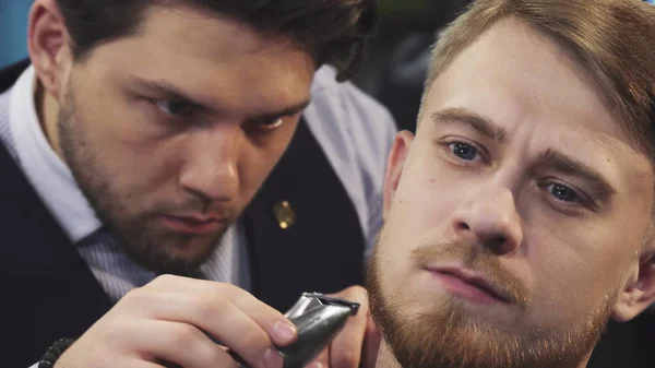 Close up of a professional barber trimming beard of a young man — Stock Photo, Image