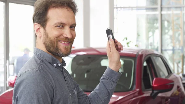 Glücklicher älterer Mann lächelt und zeigt seinen Autoschlüssel im Autohaus — Stockfoto