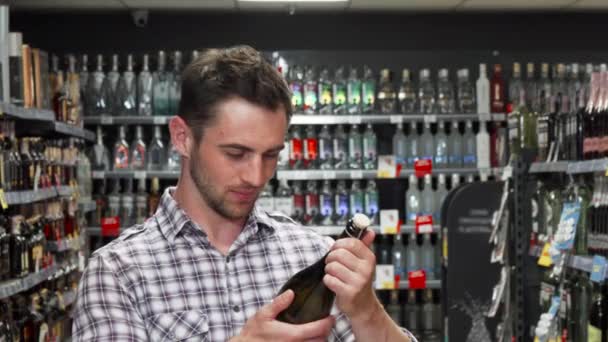 Красивый молодой человек улыбается в камеру, выбирая вино — стоковое видео