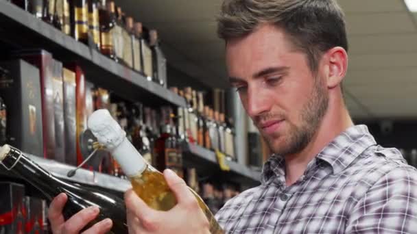 Junger Mann schaut verwirrt bei der Weinauswahl — Stockvideo