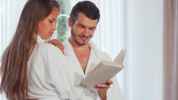 Happy couple wearing bathrobes reading a book together — Stock Video