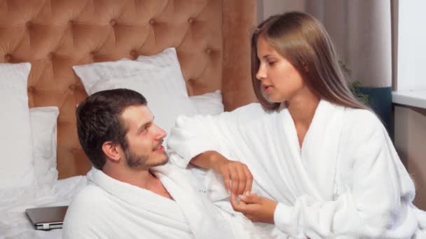 Hermosa pareja relajándose juntos en la cama, usando albornoces — Vídeo de stock