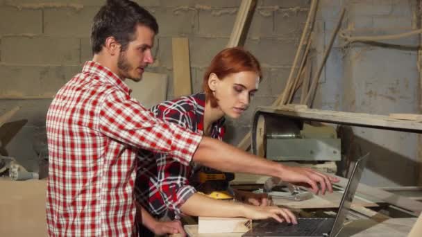 İki marangoz mobilya yaparken kendi atölyesinde dizüstü bilgisayar kullanarak — Stok video