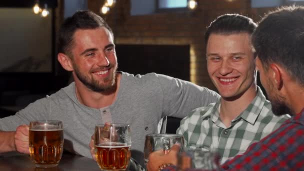 Grupo de amigos do sexo masculino batendo copos de cerveja e beber no bar — Vídeo de Stock