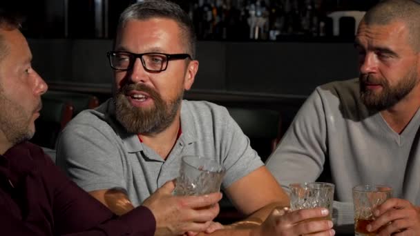 Grupp av mogen manliga vänner skrattar och pratar över glas whiskey i baren — Stockvideo