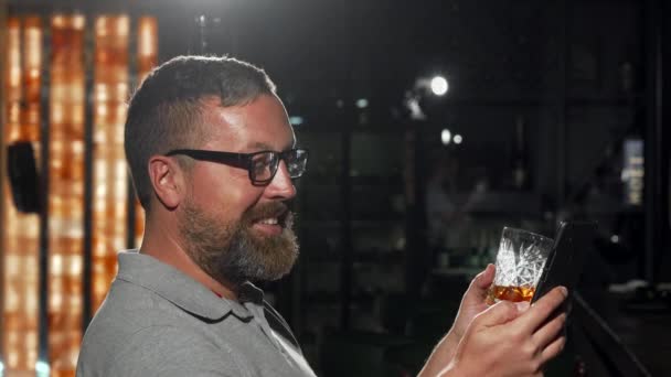 Бородатий чоловік чекає свого друга в барі, використовуючи смартфон — стокове відео