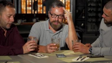 Üzgün arkadaş barda yudumlarken destekleyen iki olgun adam