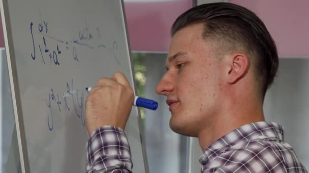 Joven guapo resolviendo problema de matemáticas en pizarra blanca — Vídeo de stock