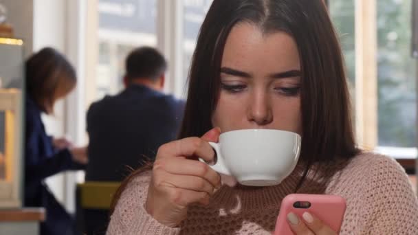 Belle femme buvant du café, en utilisant son téléphone intelligent au café — Video