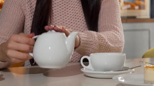 Woman pouring aromatic tea into her cup at the coffee shop