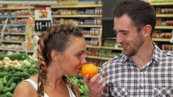 Alegre joven pareja oliendo naranjas mientras compra comida —  Fotos de Stock