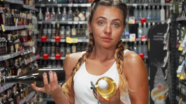 Ung kvinna ser förvirrad samtidigt plocka vin i butiken — Stockfoto