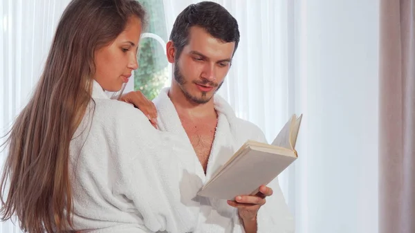 Casal feliz vestindo roupões de banho lendo um livro juntos — Fotografia de Stock