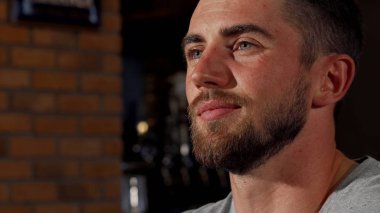 Bira yudumlarken sevinçle gülümseyen yakışıklı sakallı adam