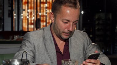 Bardaki viski tadımı sırasında akıllı telefon kullanan yakışıklı olgun adam