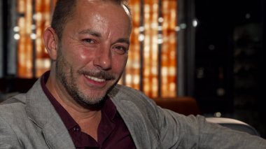 Viski yudumlarken kameraya gülümseyen yakışıklı olgun adam