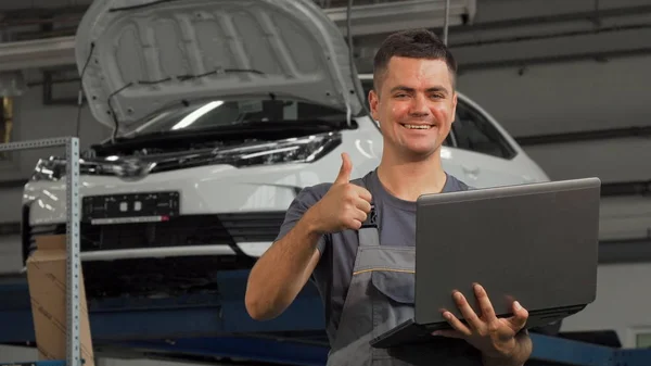 Car mechanic smiling showing thumbs up while working on the laptop