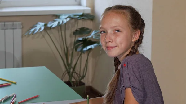 Gelukkig schattig schoolmeisje glimlachen naar de camera over haar schouder tijdens het tekenen — Stockfoto