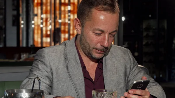 Bardaki viski tadımı sırasında akıllı telefon kullanan yakışıklı olgun adam