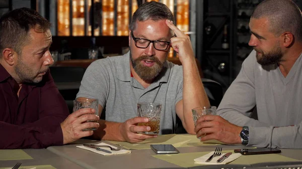 Üzgün arkadaş barda yudumlarken destekleyen iki olgun adam