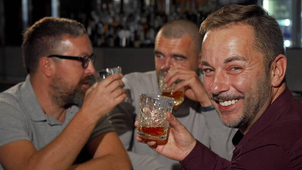 Happy mature man smiling to the camera while drinking whiskey with friends