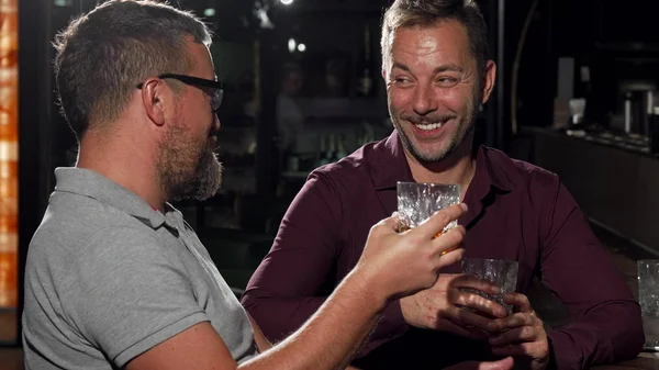 Two friends laughing to the camera while having drinks together