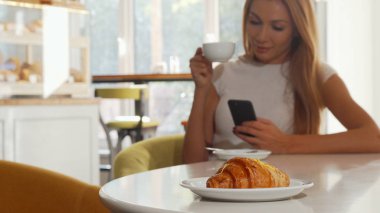 Lezzetli kruvasan, kahve dükkanında akıllı telefon kullanan kadın tarih seçici odak