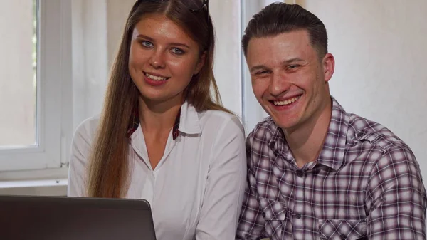 Два бізнес-колеги посміхаються до камери, використовуючи ноутбук — стокове фото