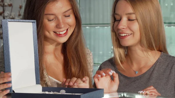 Dos hermosas amigas examinando joyas puestas en una caja para la venta en la tienda — Foto de Stock