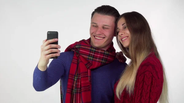 Lovely couple in warm cozy clothing taking selfies together using smart phone