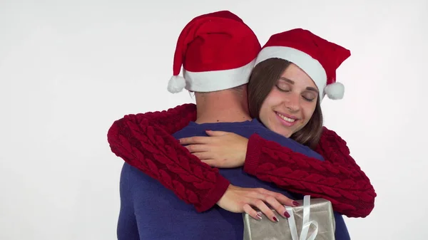 Jovem encantadora de chapéu de Natal, segurando seu presente abraçando seu homem — Fotografia de Stock