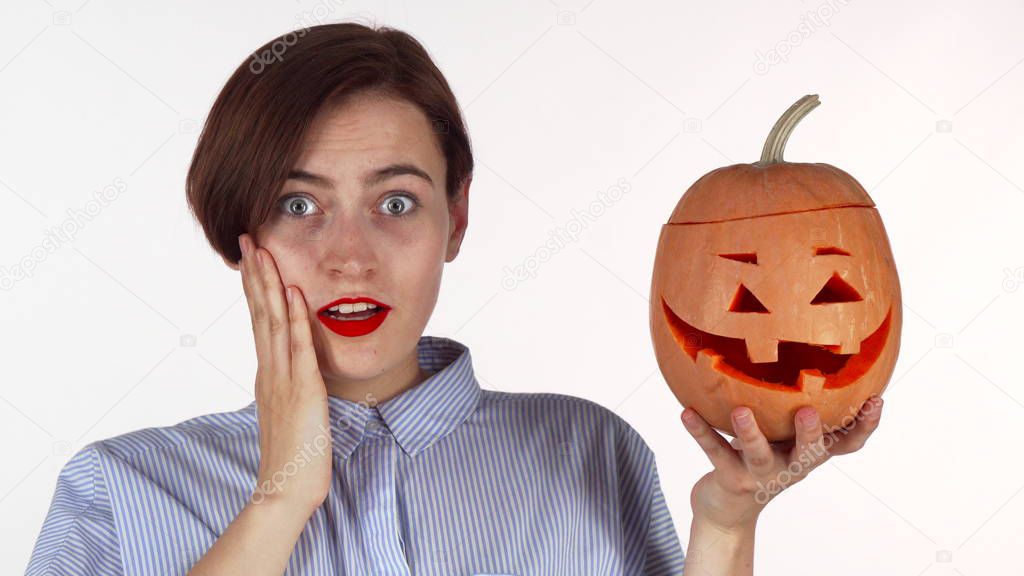 Young woman looking shocked, posing with halloween carved pumpkin