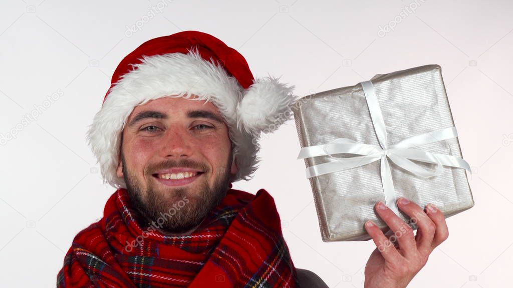 Handsome bearded man in Christmas hat smiling, holding up a present