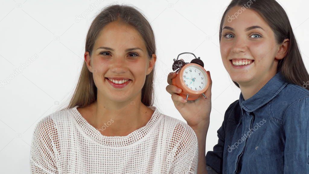 Young woman waking up her sleepy friend with an alarm clock