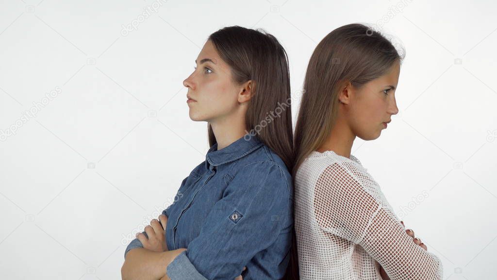 Two female friends standing back to back looking angry after having a fight