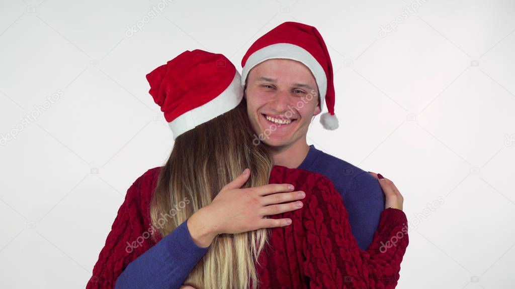 Handsome young man wearing Christmas hat hugging his girlfriend
