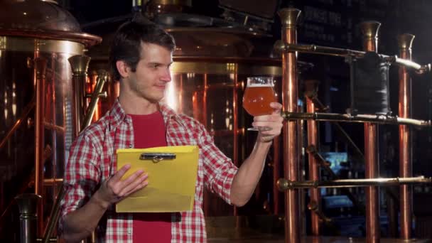 Jovem com prancheta trabalhando na cervejaria artesanal, examinando cerveja — Vídeo de Stock