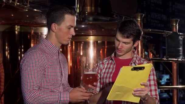 Два пивовара осматривают ремесленное пиво, работают на пивоварне — стоковое видео