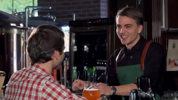 Щасливий чоловік розмовляє з барменом, маючи пиво в місцевому пабі — стокове відео