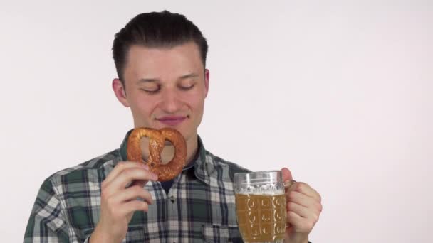 Jovem atraente homem rindo alegremente, bebendo cerveja deliciosa, segurando um pretzel — Vídeo de Stock